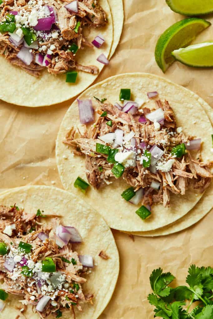 Three tacos on corn tortillas topped with Instant Pot carnitas, jalapeno, red onion, and cojita cheese. 