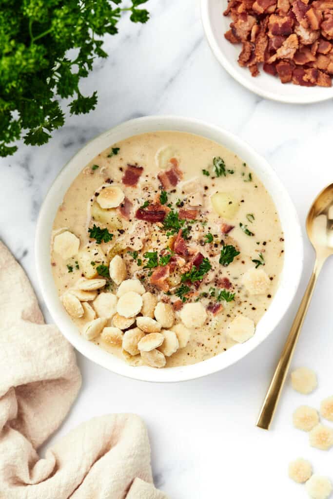 A bowl of Instant Pot clam chowder with parsley and chopped bacon placed around it.