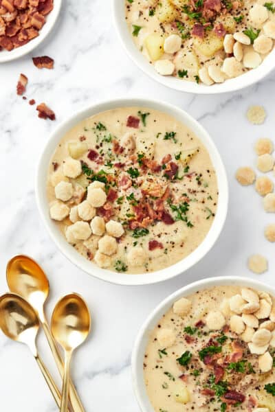Three bowls of Instant Pot clam chowder topped with bacon, parsley, black pepper, and oyster crackers.