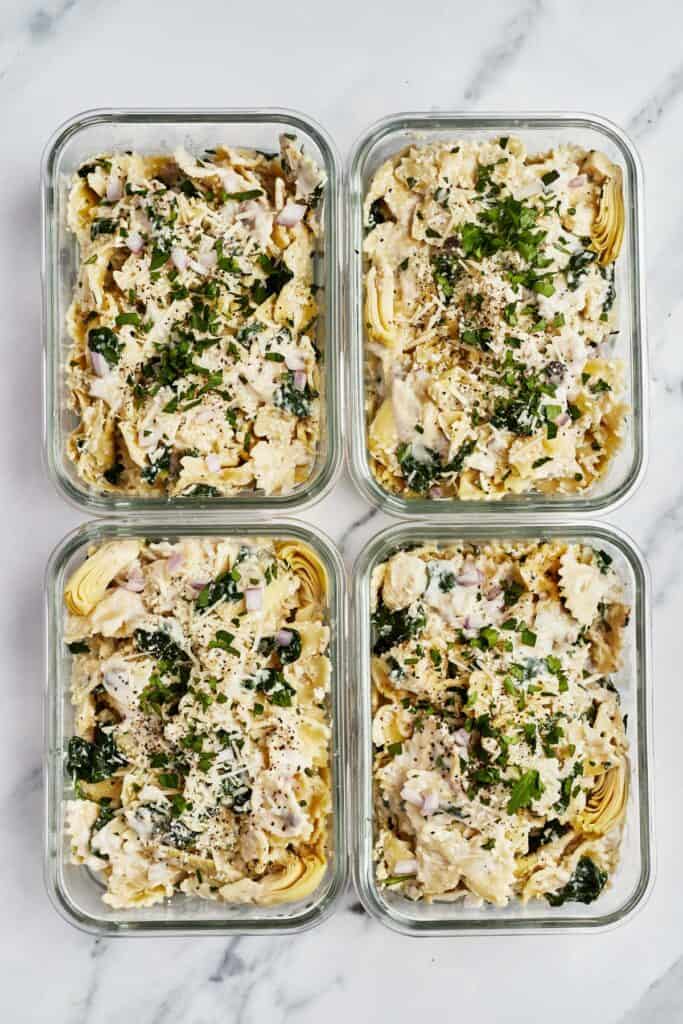 Four meal prep containers, each filled with Instant Pot spinach artichoke pasta.