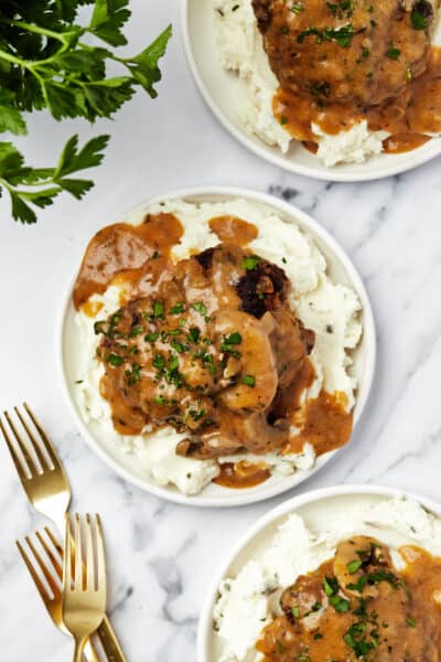 Three plates topped with mashed potatoes, Instant Pot salisbury steak, and mushroom gravy.