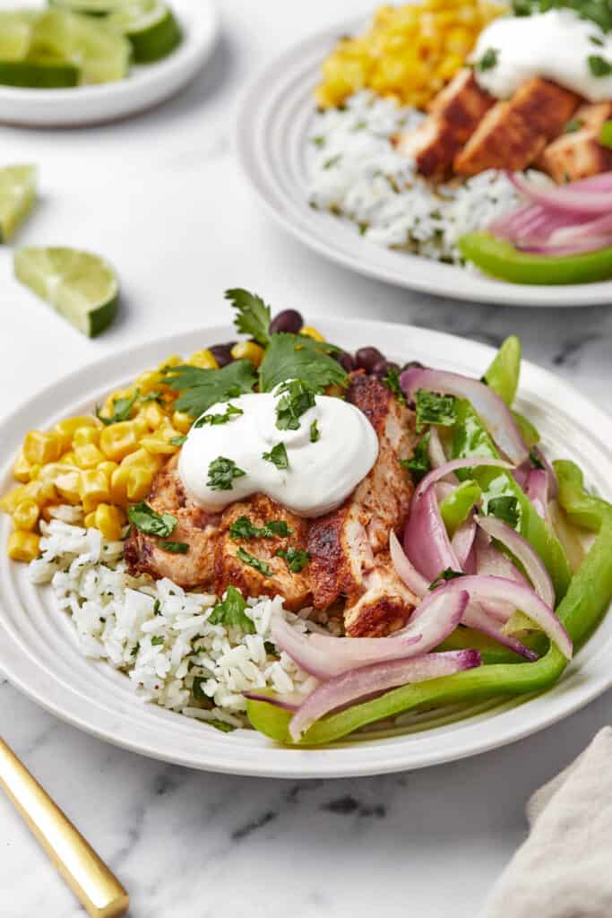 A close-up shot of a burrito bowl with a base of Instant Pot cilantro lime rice, topped with chicken, peppers, onion, black beans, corn and sour cream.