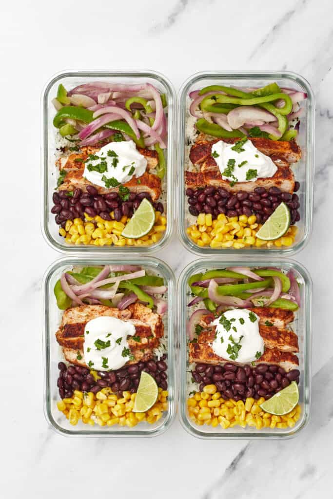 Four meal prep containers, each with a base of Instant Pot cilantro lime rice, topped with chicken, peppers, onion, black beans, corn and sour cream.