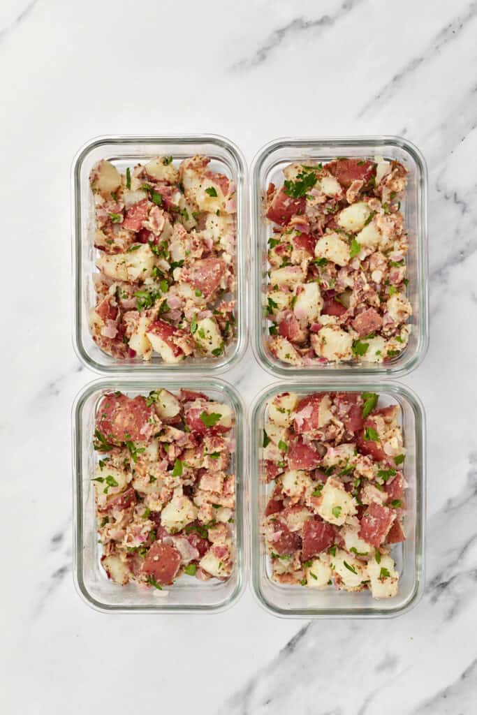 Four meal prep containers, each filled with Instant Pot German potato salad.