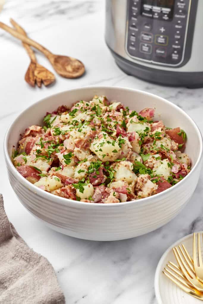 A big bowl of Instant Pot German potato salad in the foreground with an Instant Pot in the background.