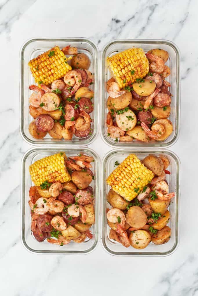 Four meal prep containers, each filled with Instant Pot cajun shrimp boil.