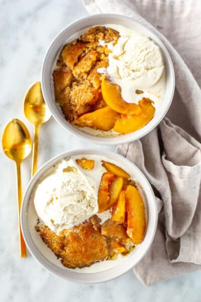 Two bowls of Instant Pot peach cobbler with ice cream on top.